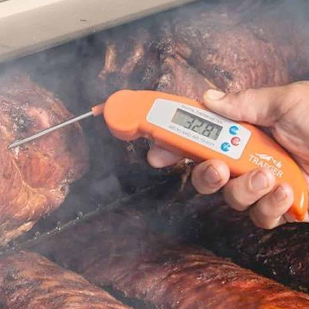 An orange meat thermometer checking the internal temperature of grilled meat.