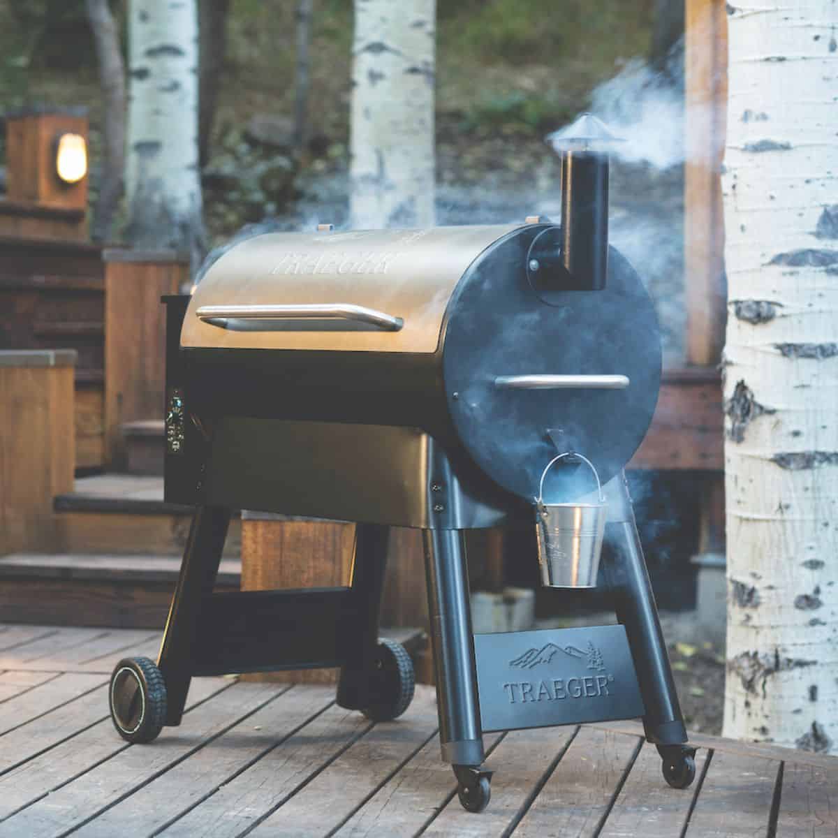 A treager smoker on a deck surrounded by trees.