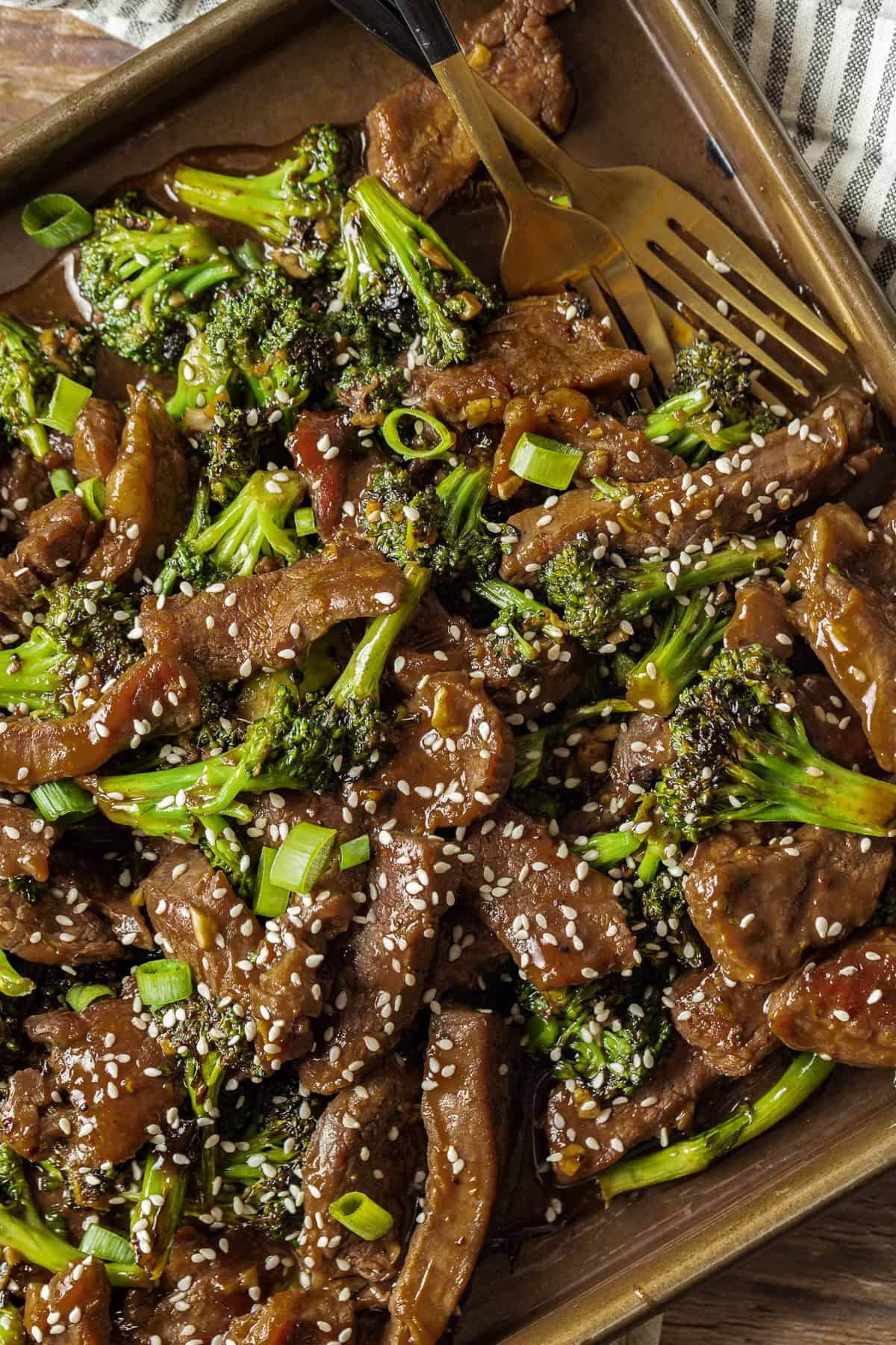 An overview shot of beef and broccoli topped with green onions and sesame seeds on a baking sheet.
