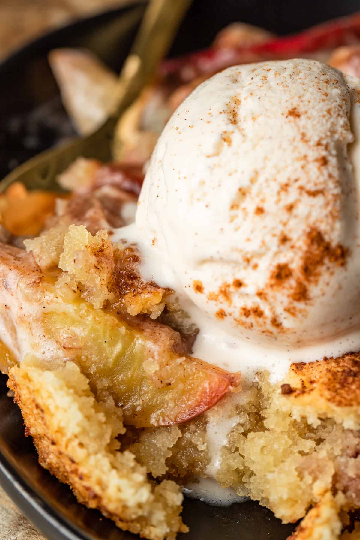 Peach cobbler in a cast iron skillet topped with a scoop of melting ice cream and cinnamon.