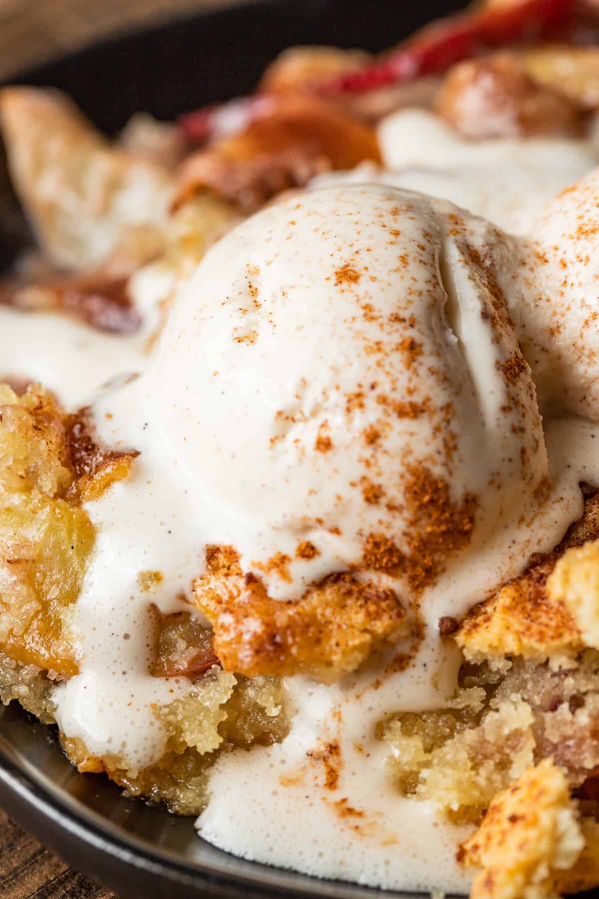 Peach cobbler in a cast iron skillet topped with a scoop of melting ice cream and cinnamon.