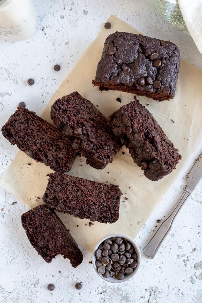 An overview shot of slices of banana bread next to chocolate chops and a knife