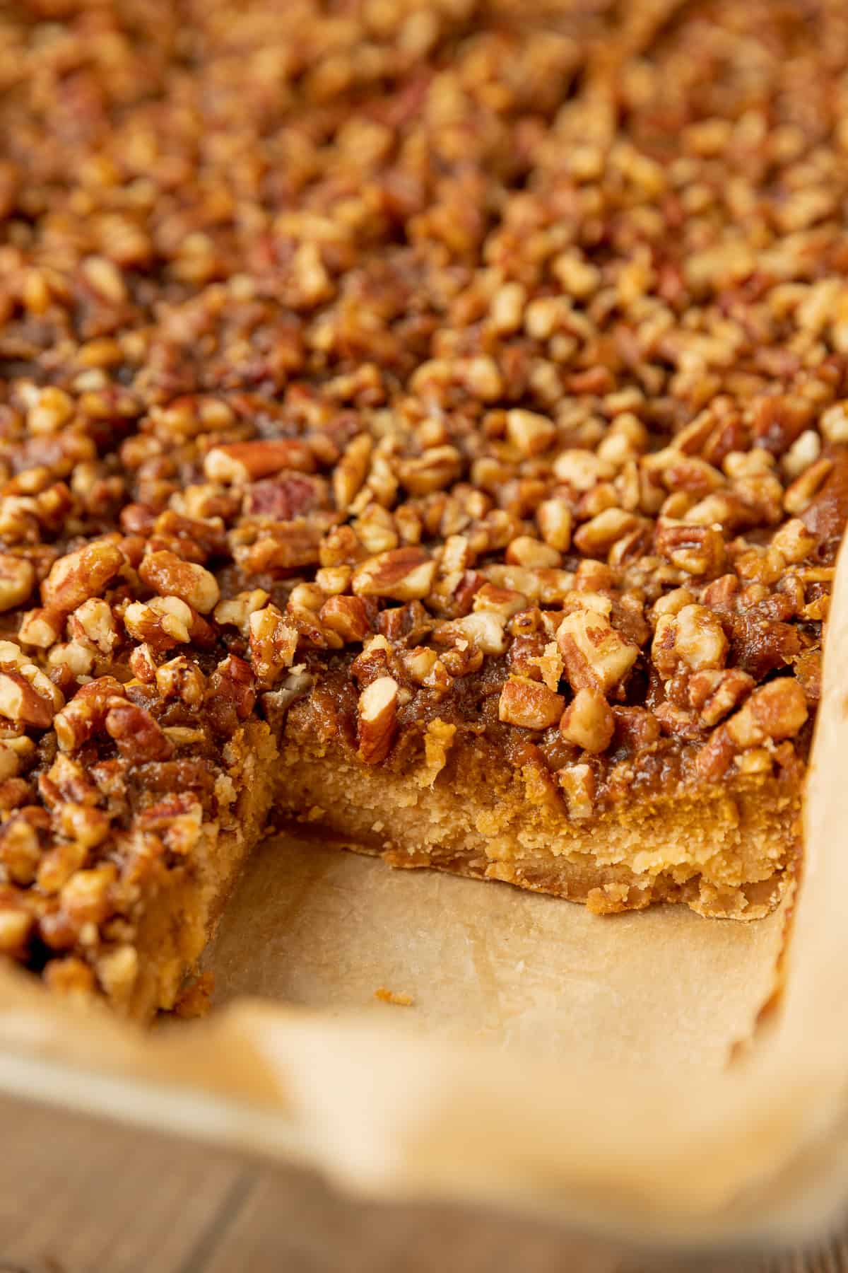 Pumpkin pecan pie bars in a pan with one corner piece missing showing the three layers.