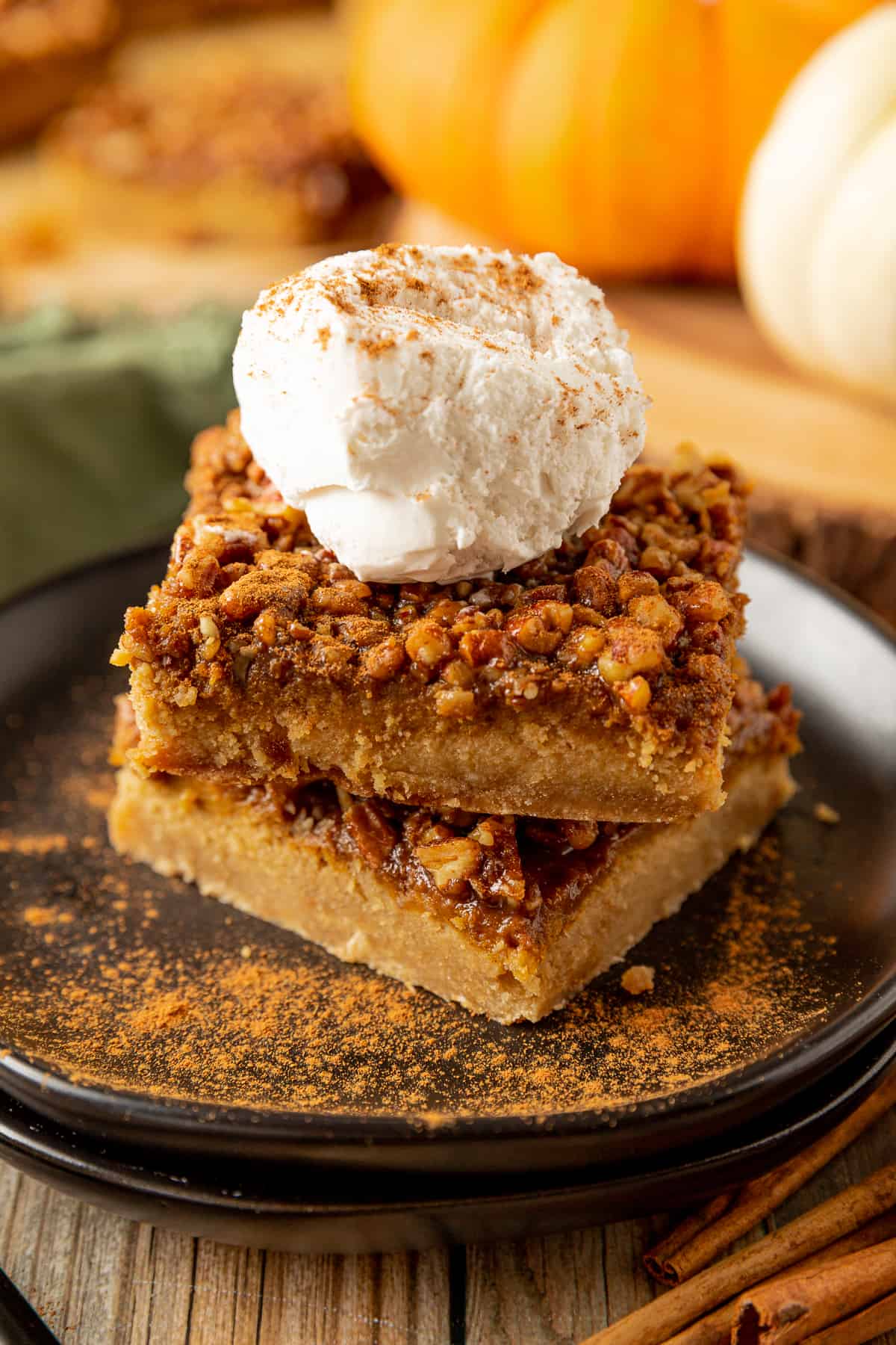 A stack of pumpkin pecan pie bars on a black plate topped with whipped cream and pumpkin pie spice