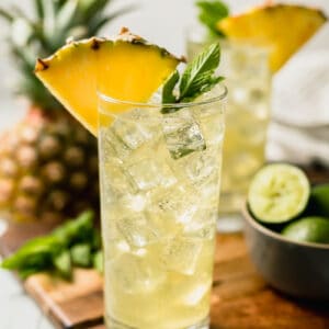 Two pineapple mojito mocktails on a cutting board topped with pineapple and mint