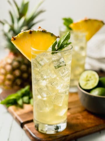 Two pineapple mojito mocktails on a cutting board topped with pineapple and mint