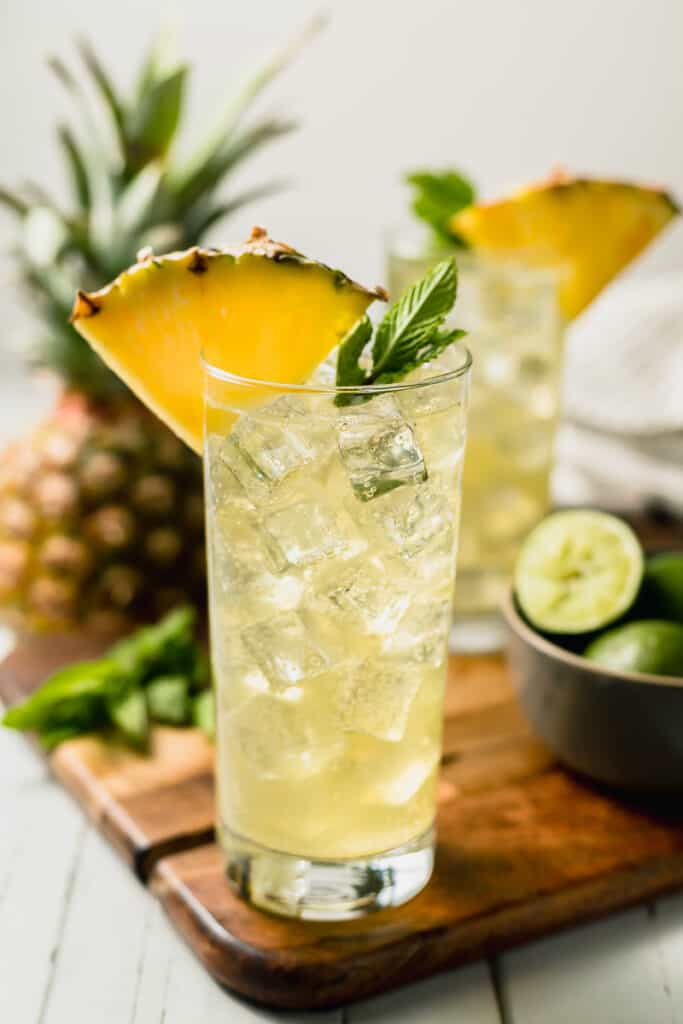 Two pineapple mojito mocktails on a cutting board topped with pineapple and mint