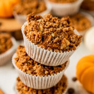 A stack of paleo pumpkin chocolate chip muffins on a white wood background near cinnamon sticks and chocolate chips