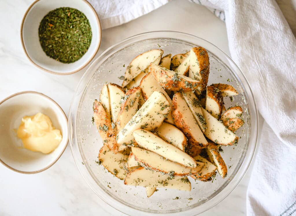 Potato wedges in a bowl with seasonings and ghee