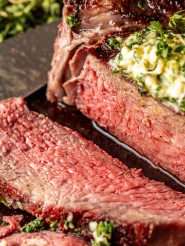 A reverse seared tomahawk steak sliced open and topped with an herb butter compound.