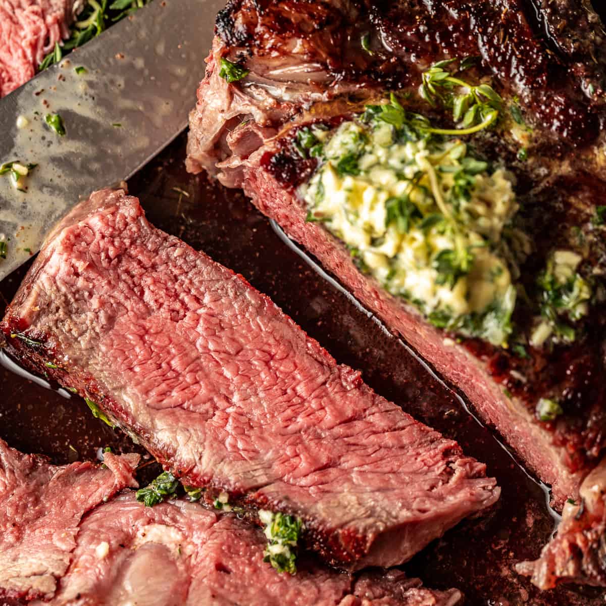 A reverse seared tomahawk steak sliced open and topped with an herb butter compound.