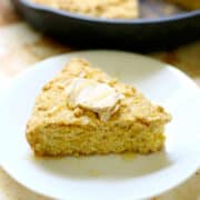 A slice of Rustic Gluten-Free Cornbread on a white plate topped with butter.