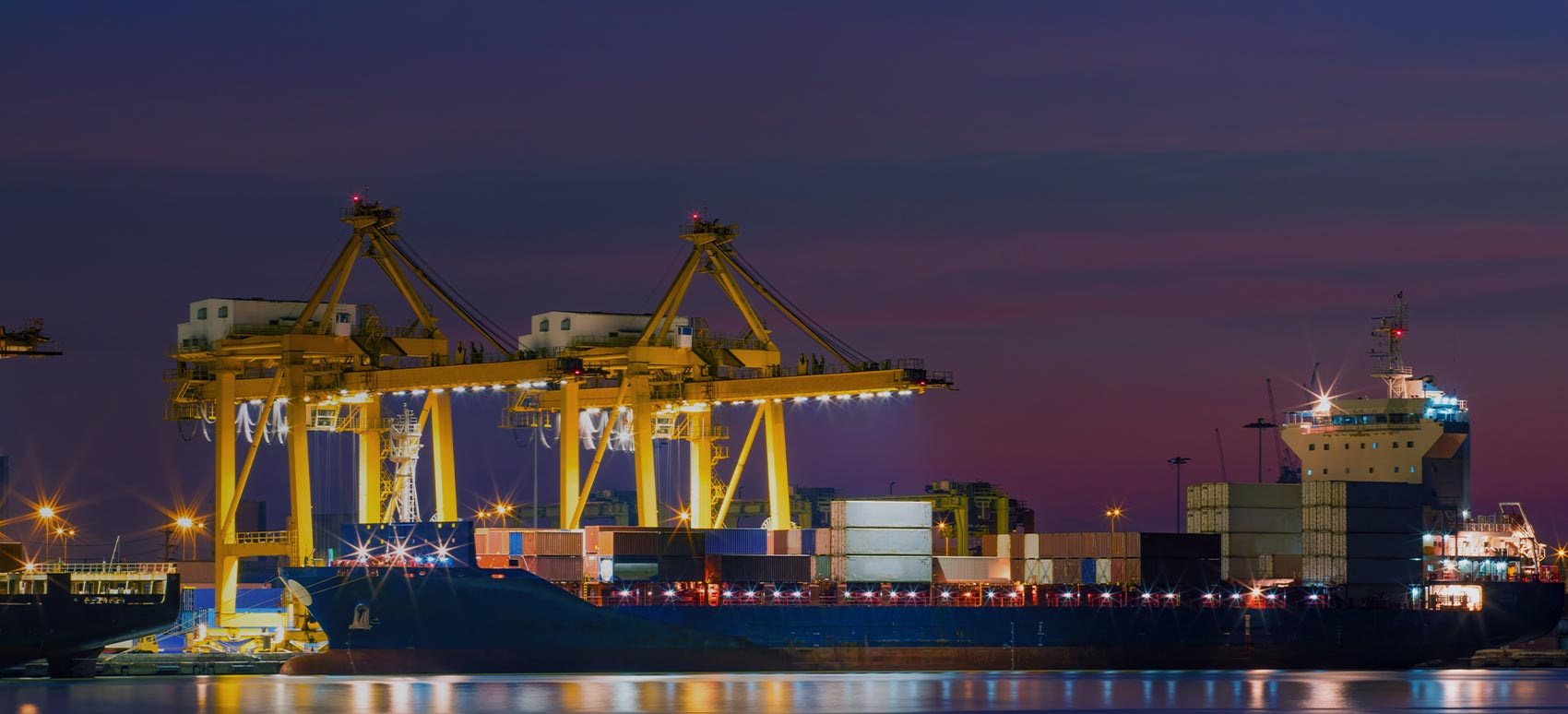Nighttime port with cargo ship and cranes.