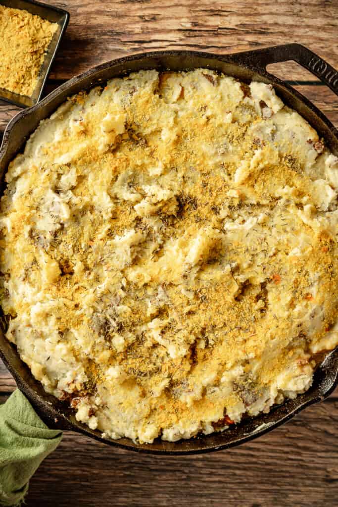 An overview shot of shepherds pie ready to be baked in a cast iron pan on a wood background