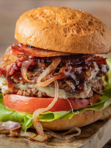 Two smash burger patties between a hamburger bun topped with lettuce, tomato, bbq sauce, and onions.