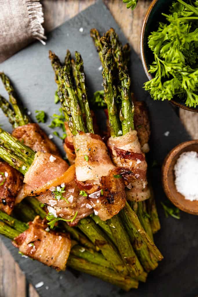 An overview shot of smoked bacon wrapped asparagus on a serving board.