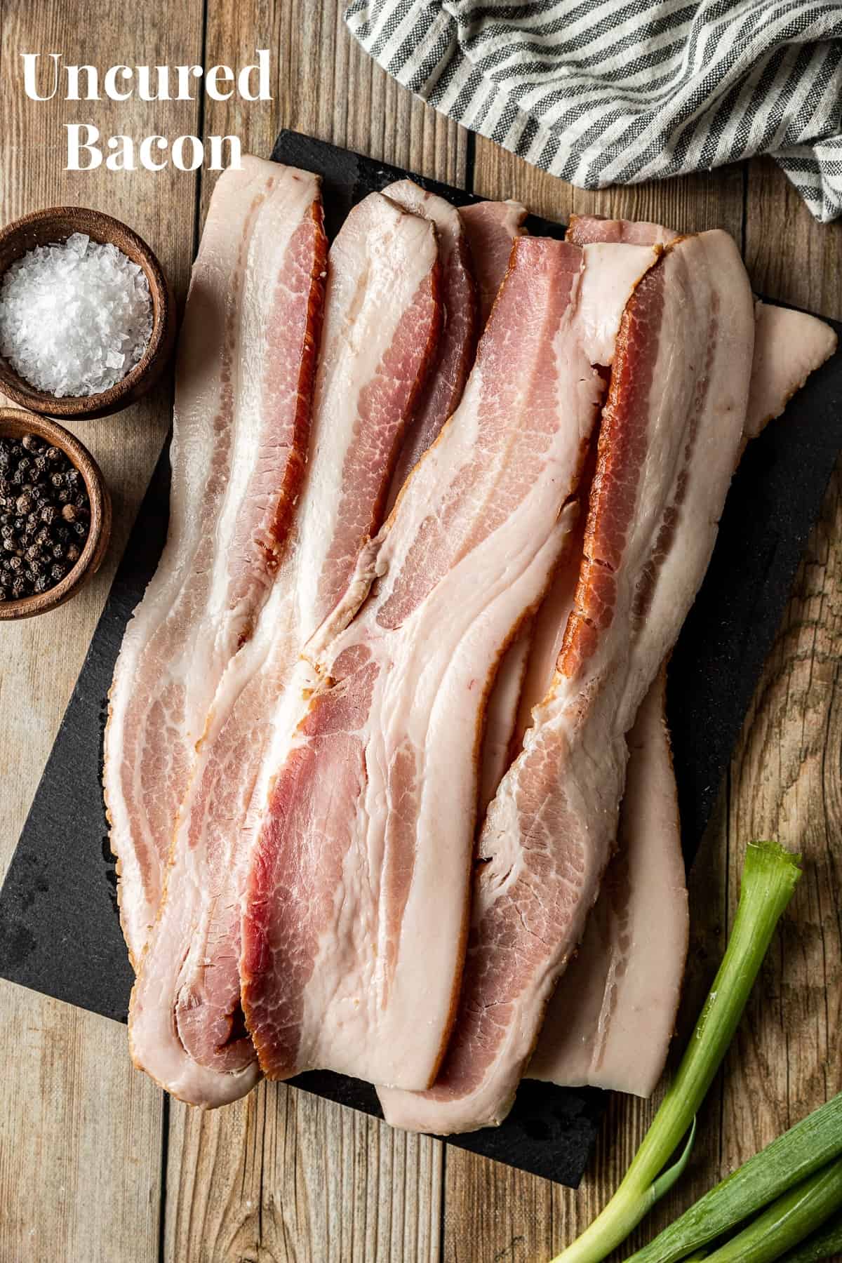 An overview shot of raw bacon slices on a black cutting board..