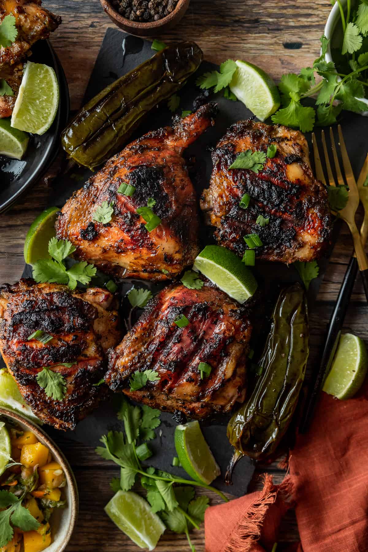 Jerk chicken thighs topped with cilantro and lime wedges on a black cutting board