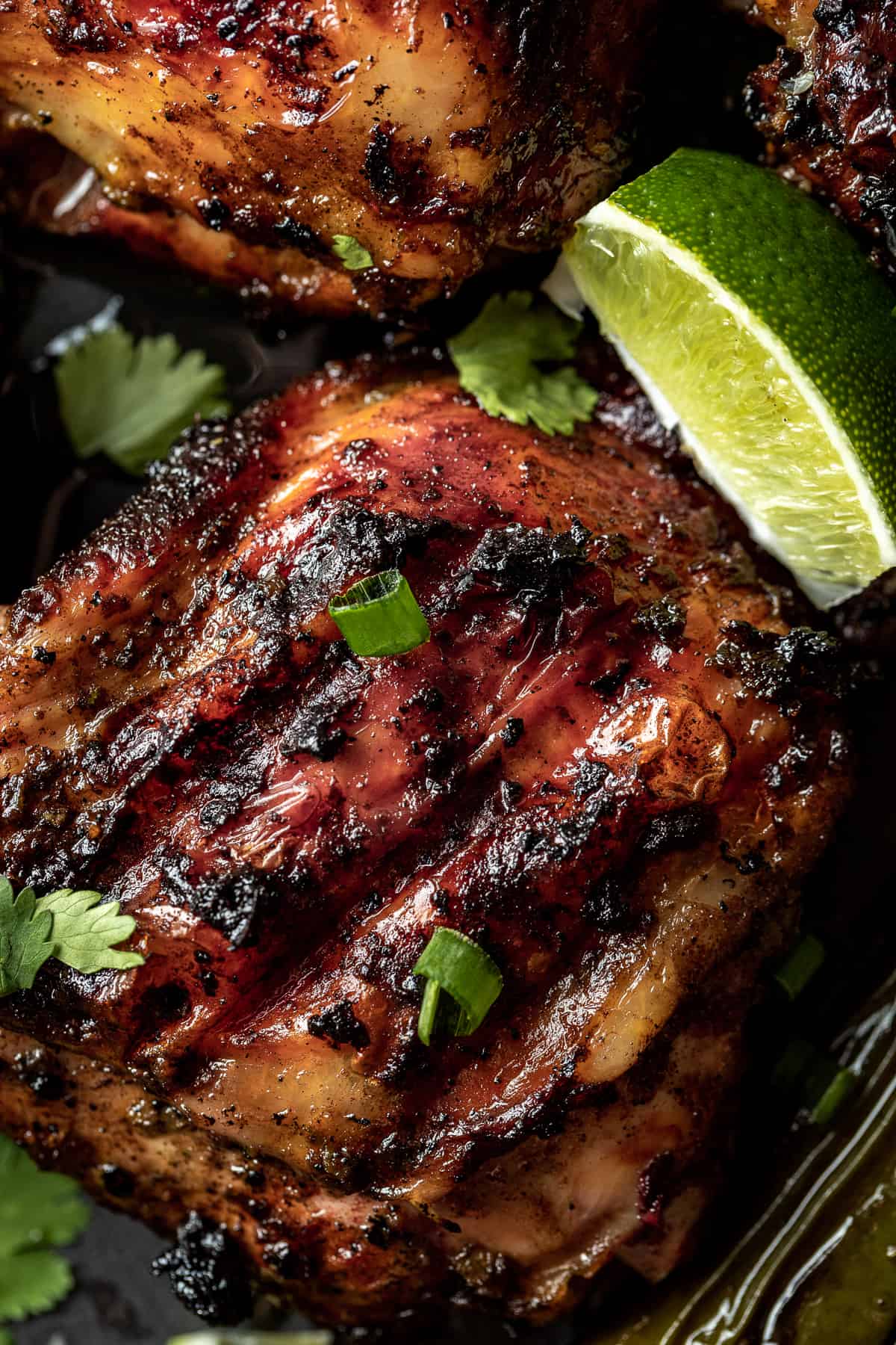 A close up image of a grilled jerk chicken thigh topped with cilantro and lime wedges.