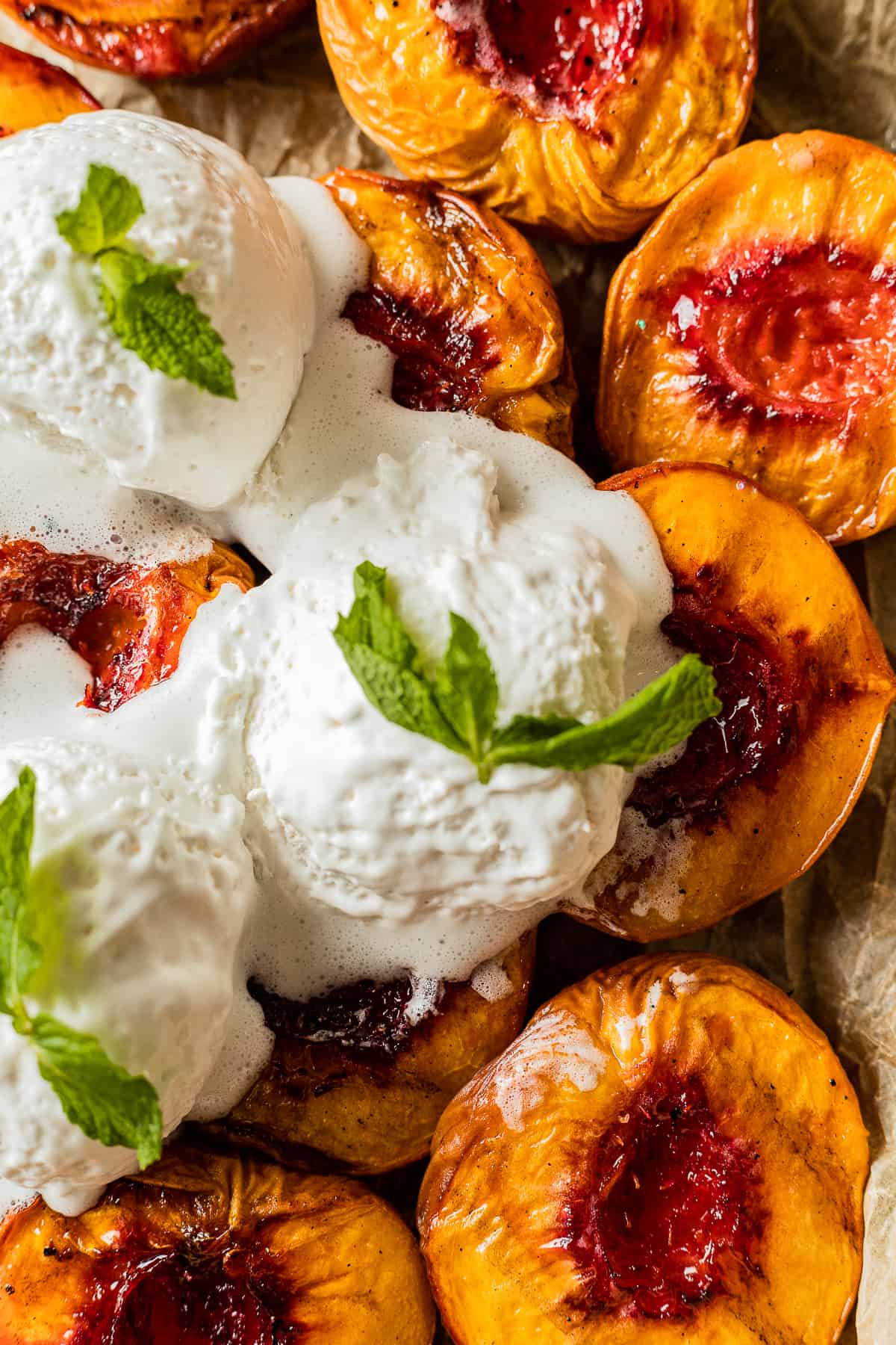 Smoked peaches with grill marks on a baking sheet topped with vanilla ice cream and mint leaves.