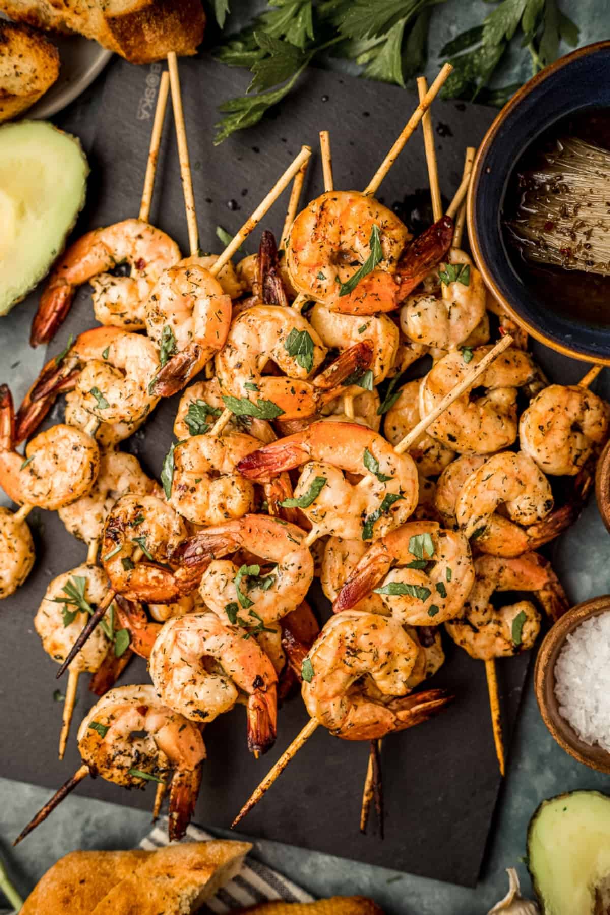 An overhead shot of smoked shrimp skewers on a black serving board next to Whole30 marinade and garnishes