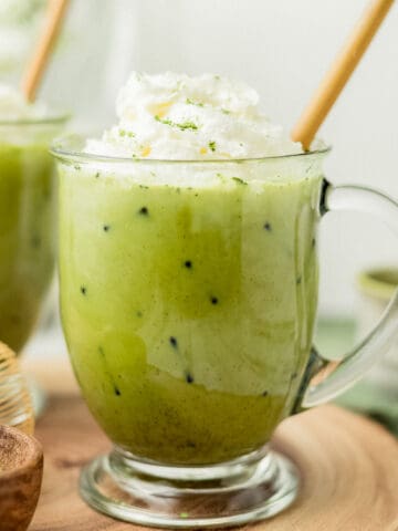 A glass of iced matcha latte topped with whipped cream on a wooden board.