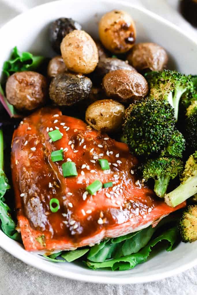 A bowl of teriyaki salmon with roasted potatoes and brocolli.