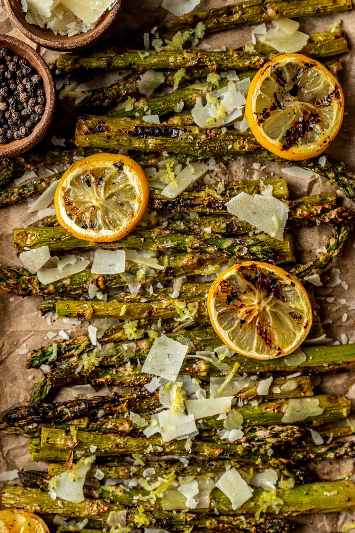 An overview shot of grilled asparagus spears topped with grilled lemon, parmesean cheese, and cracked black pepper.