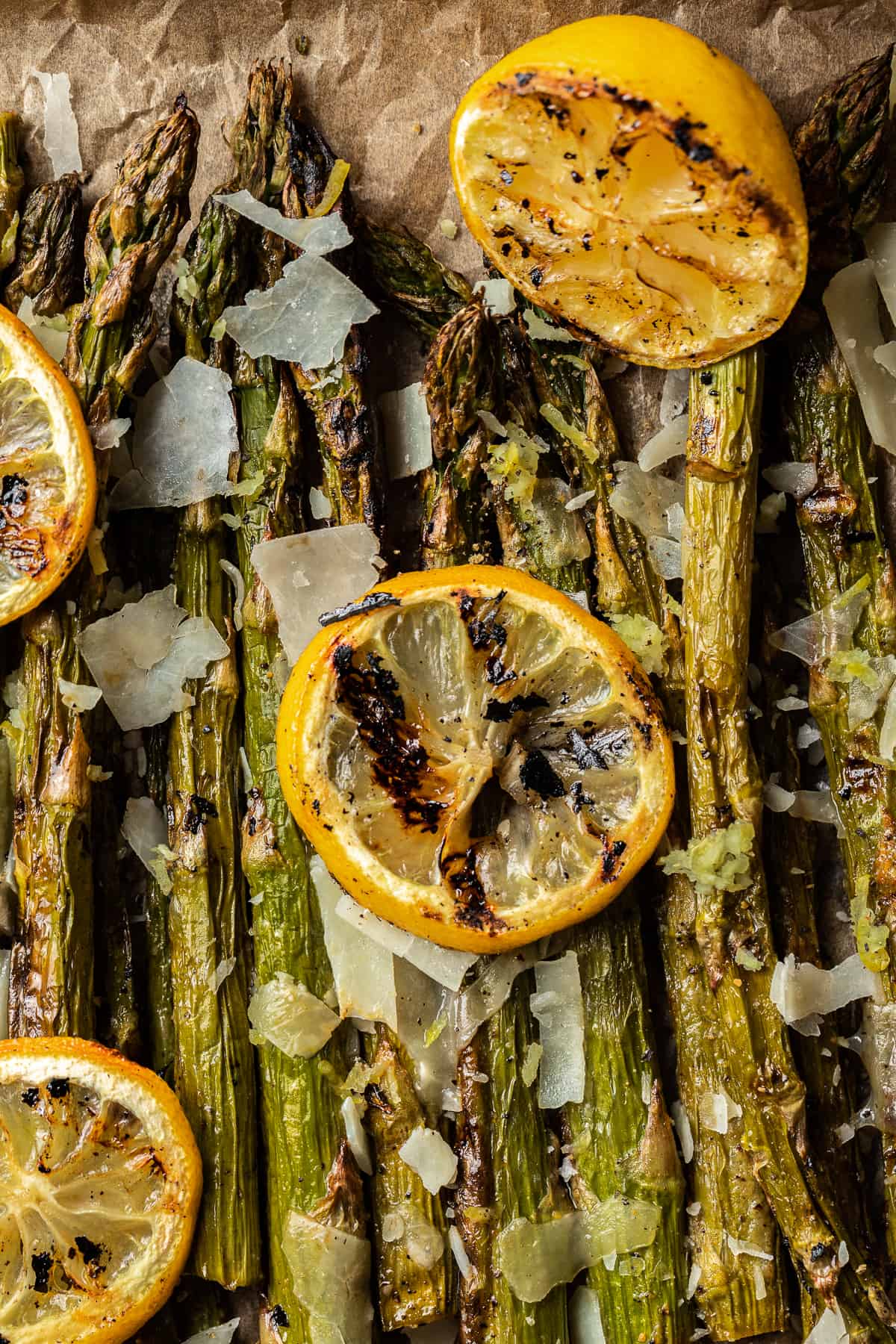 An overview shot of grilled asparagus spears topped with grilled lemon, parmesean cheese, and cracked black pepper.