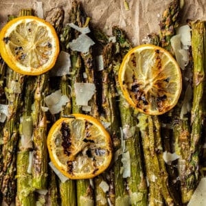 An overview shot of grilled asparagus spears topped with grilled lemon, parmesean cheese, and cracked black pepper.