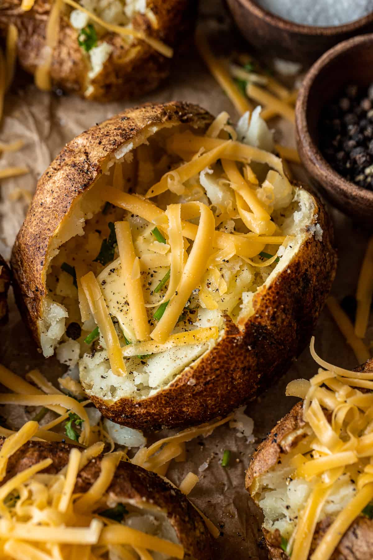 An overview shot of smoked baked potatoes filled with melted butter, chives, parsley, and shredded cheese on parchment paper.