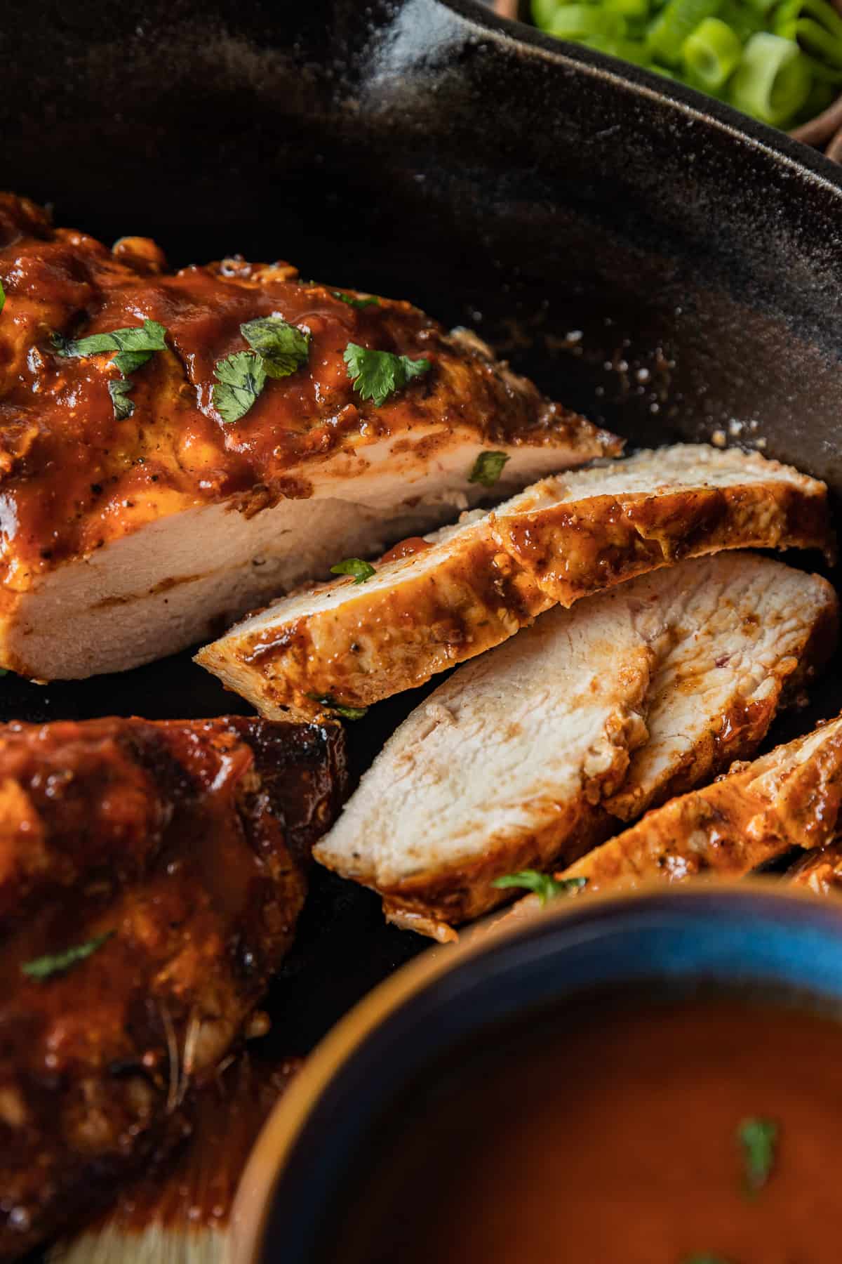A close up shot of sliced BBQ chicken in a cast iron pan topped with parsley.