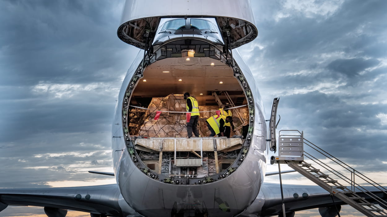 A cargo plane with its front hatch open is being loaded with cargo.