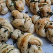 Vegan garlic knots on a white background topped with herbs and roasted garlic.
