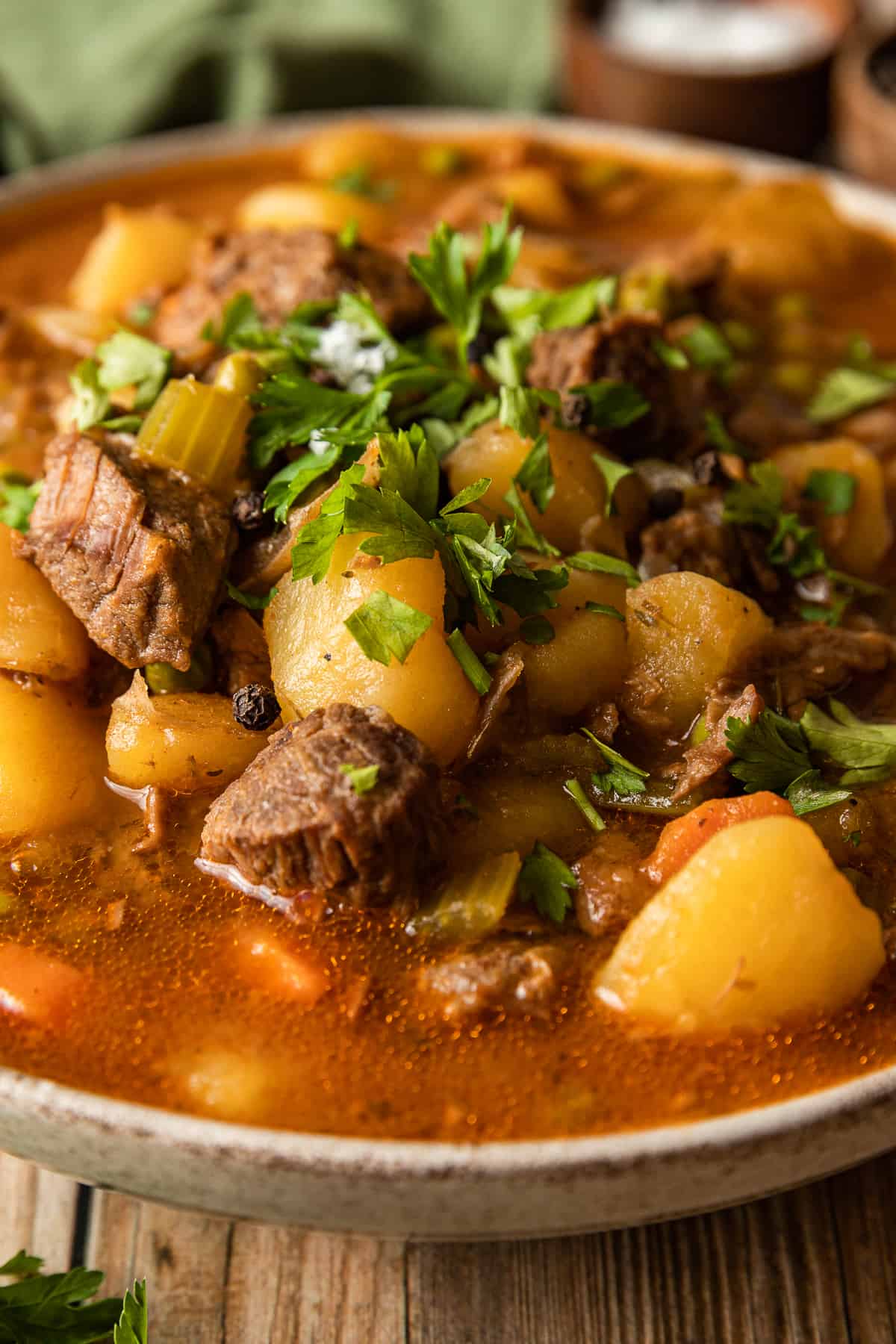 A close up view of beef stew with chuck roast and potatoes in a serving bowl topped with parsley.