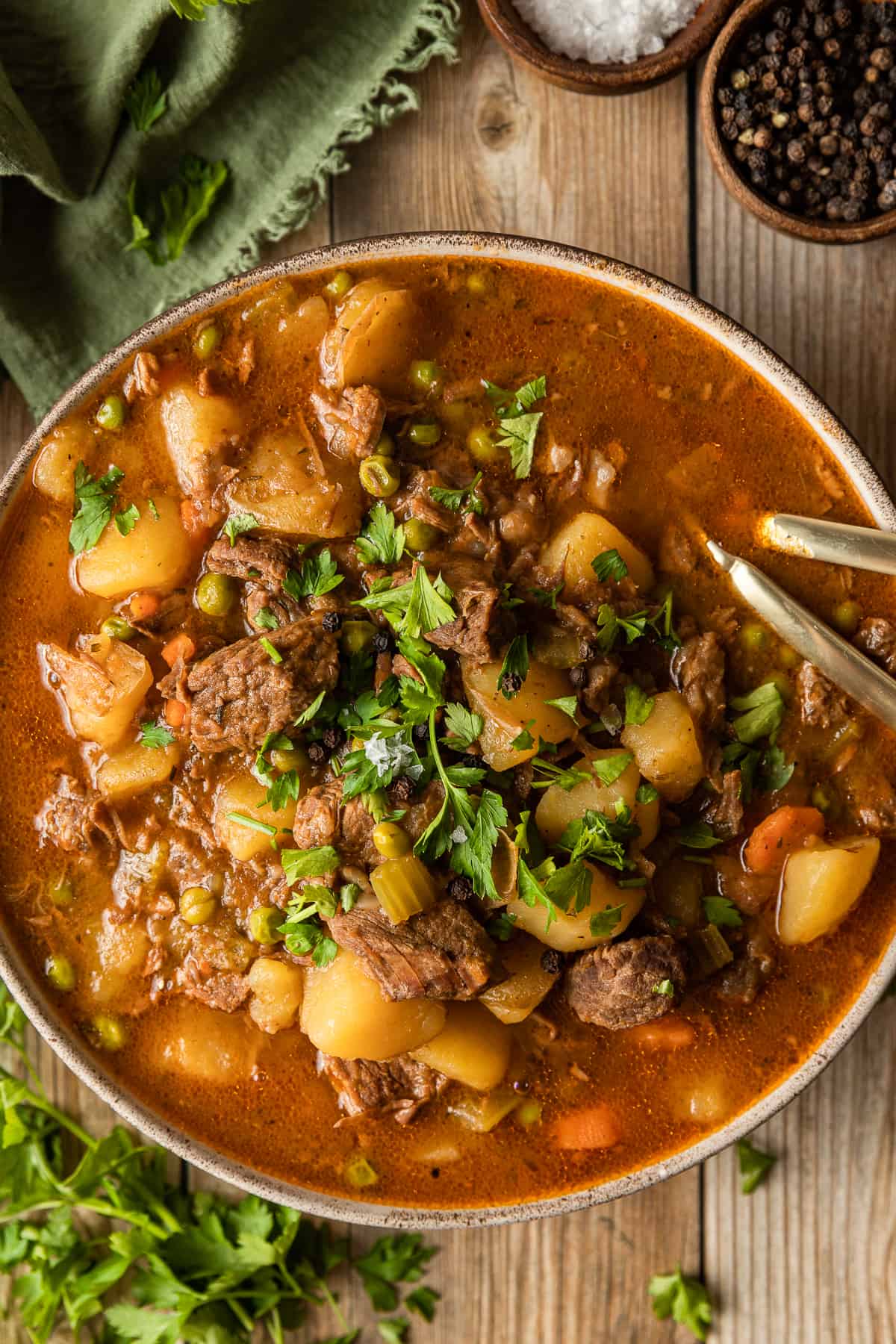 An overview shot of a bowl of beef stew on a wood background near a green linen.