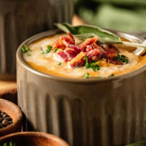 A bowl of Butternut Squash Soup topped with coconut cream, bacon, and fresh sage on a wood background
