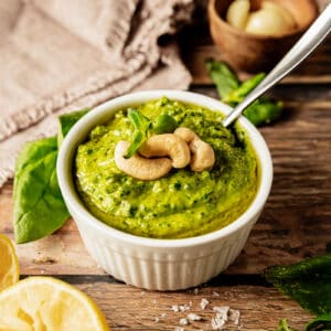 A bowl of whole30 pesto topped with cashews and olive oil on a wood background