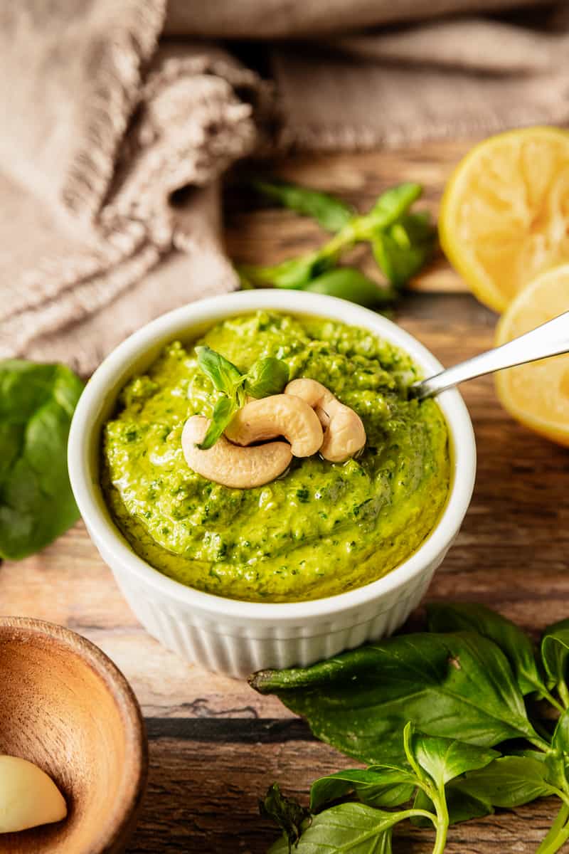 A bowl of whole30 pesto topped with cashews and olive oil on a wood background