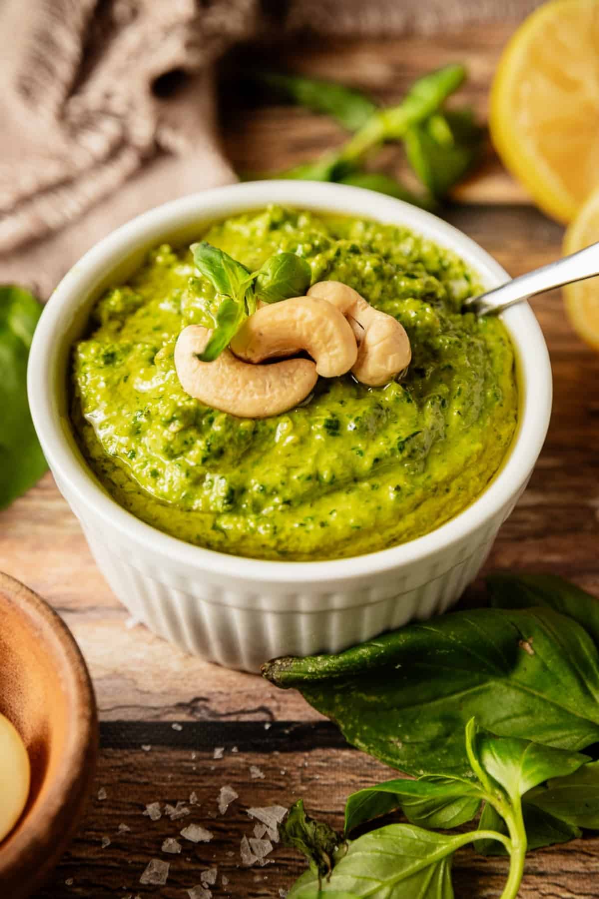 A bowl of whole30 pesto topped with cashews and olive oil on a wood background